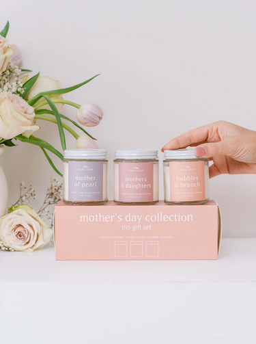 A hand reaches for one of three small jars of candles labeled